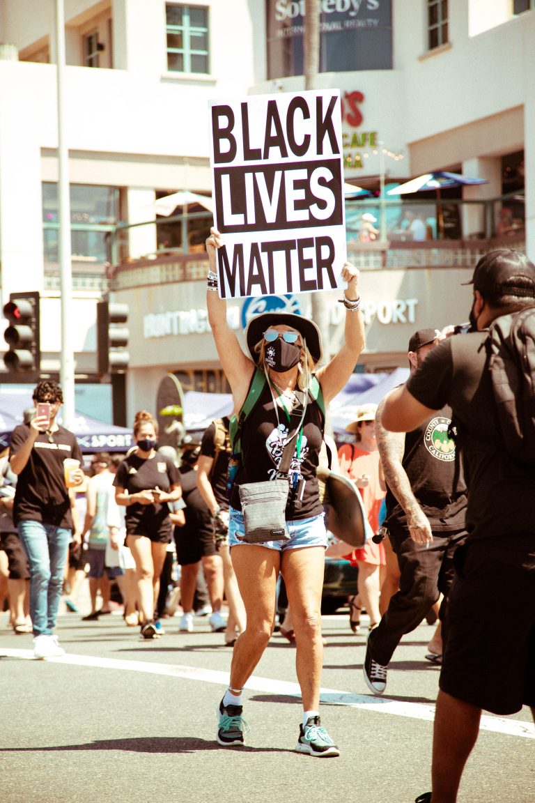 Woman in hat holding Black Lives Matter sign in front of Huntington Surf and Sport