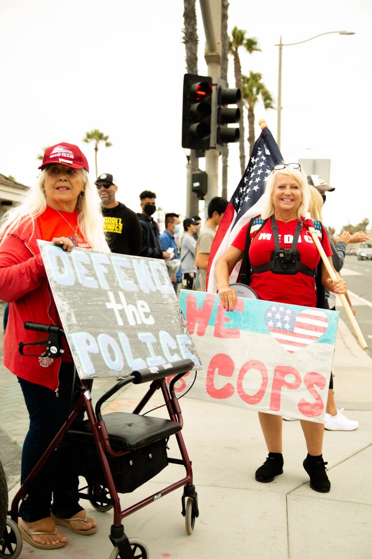 Two blonde women wearing red holding Defend the Police signs, anti-protesters, anti-BLM